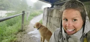 Linda steht unter einer Brücke, es regnet. Im Hintergrund ist ein Labrador zu sehen